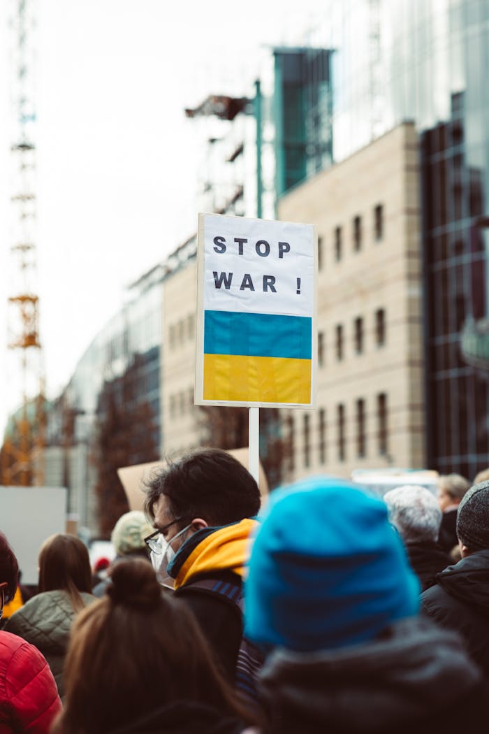 A diverse group of people protesting against war with a focus on a 'Stop War!' sign featuring Ukrainian colors.