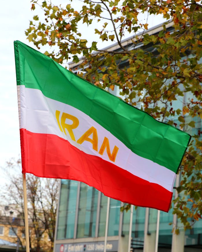 about-img Iranian flag in vibrant colors waves against an urban backdrop, capturing national pride.