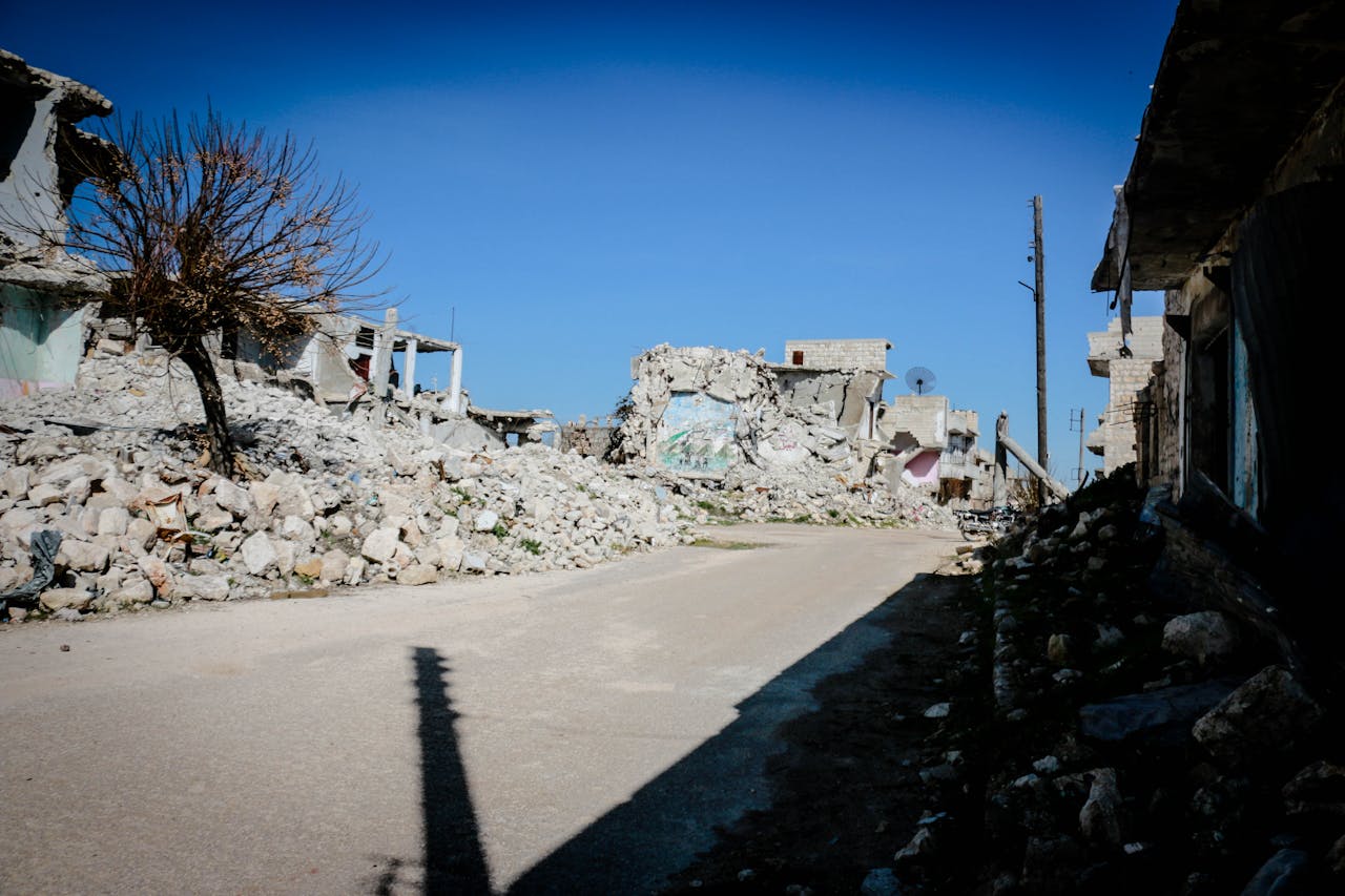 services-img Destroyed buildings and rubble in a deserted street of Idlib, Syria, under clear blue sky.